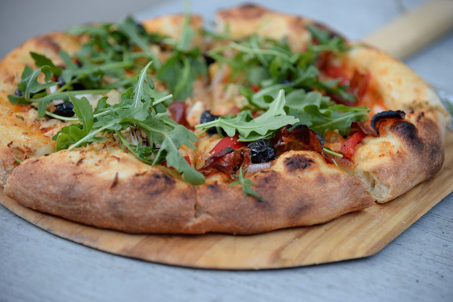 A blistered wood-fired pizza topped with arugula on a wooden peel